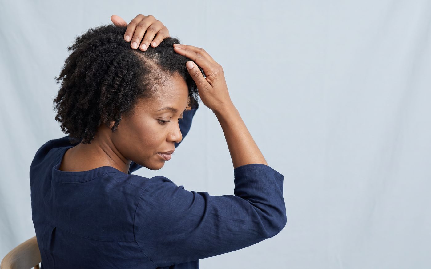 Donna che separa i capelli sulla riga centrale per mostrare il diradamento femminile