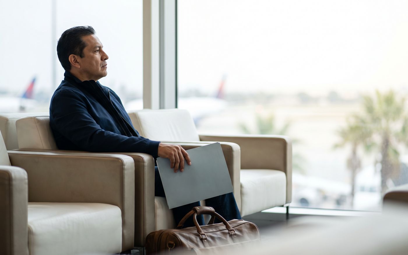Viaggiatore in sala d'attesa dell'aeroporto con una cartellina, in viaggio per il trapianto di capelli